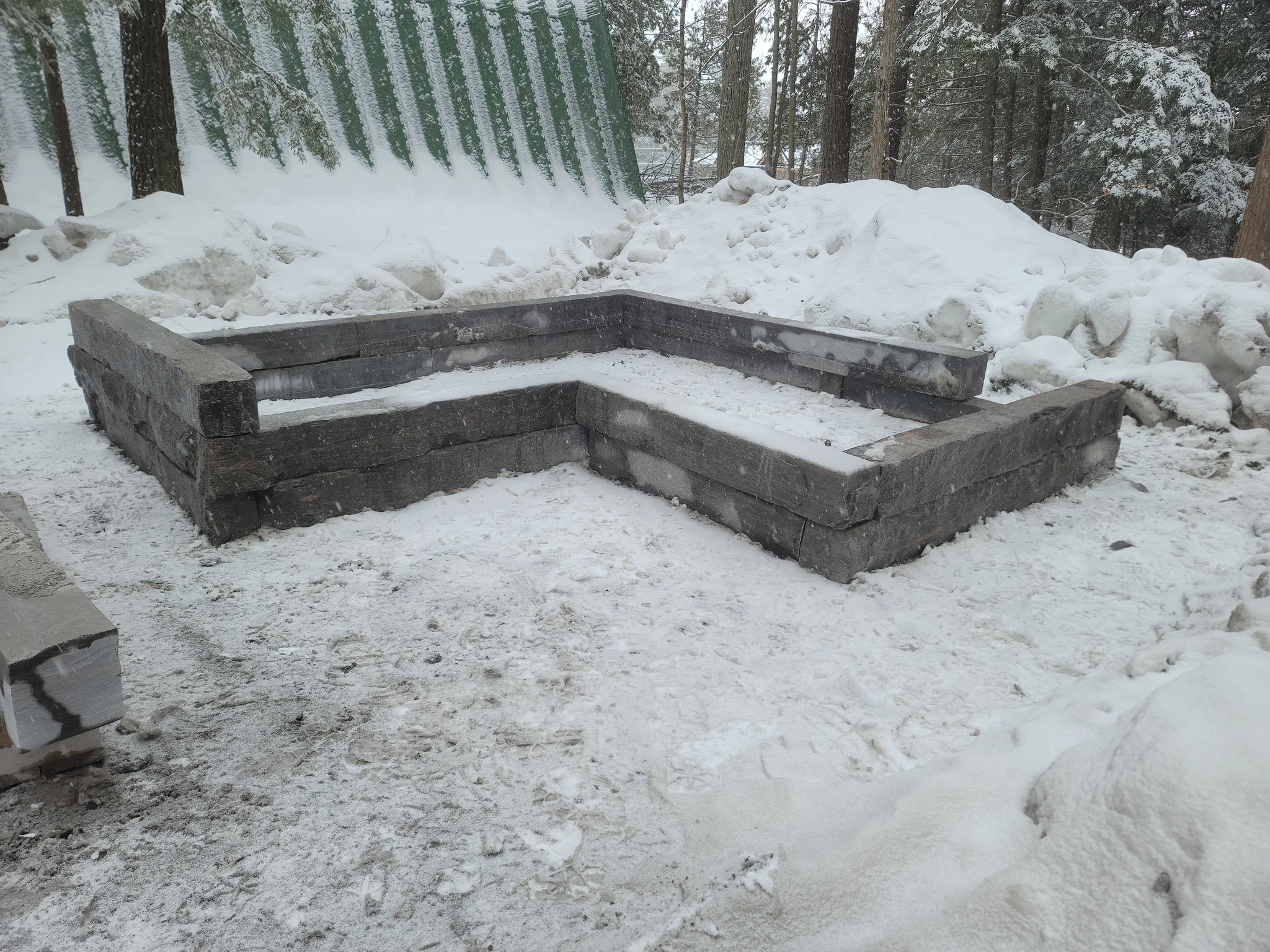 L-shaped granite planter wall under construction in a snowy Muskoka setting
