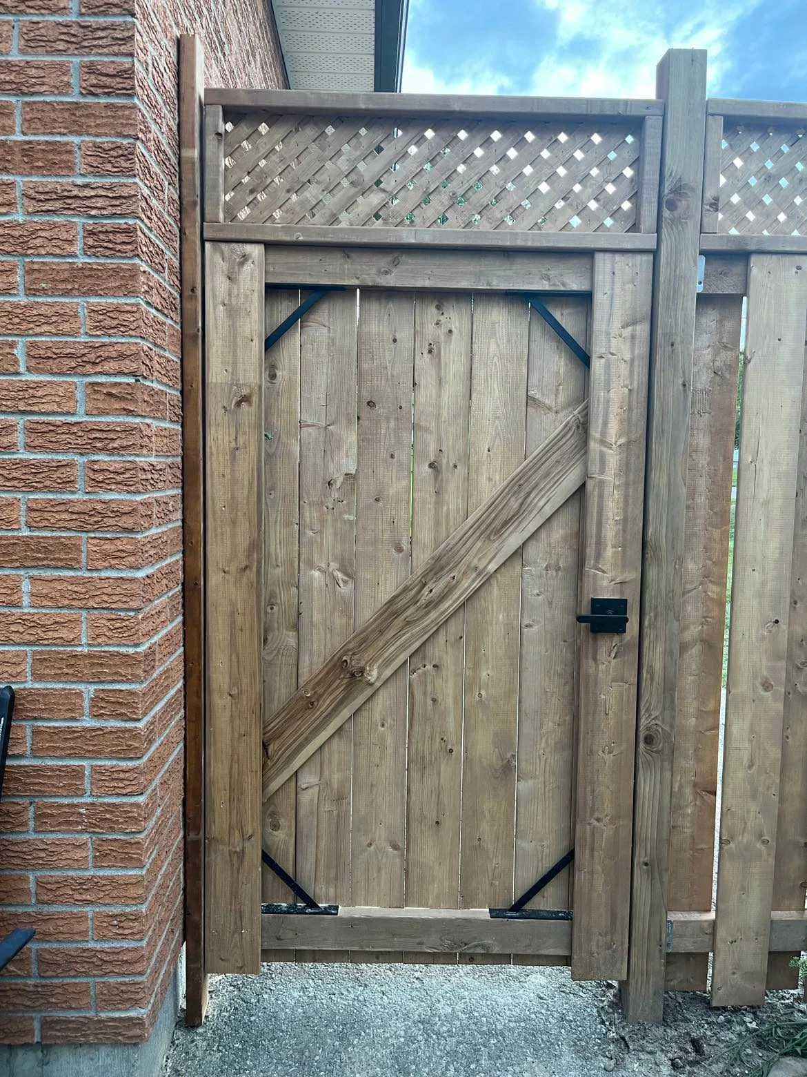 Completed gate with diagonal wood bracing, black supports, and latch hardware